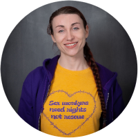 Jelena Vermilion wearing a yellow tshirt with purple text in a heart that says "Sex workers need rights not rescue"